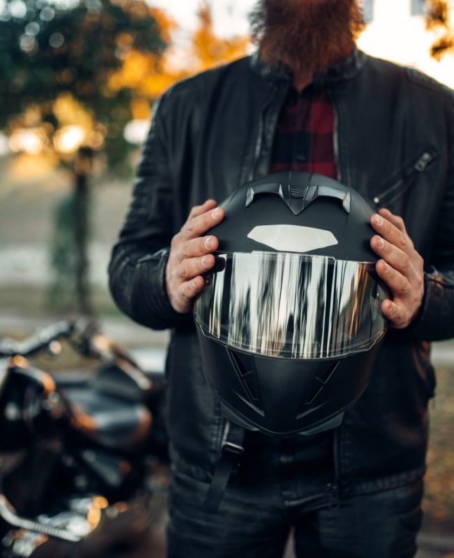 Male biker holds helmet in hands, classical chopper on background. Vintage bike, road rider and his motorcycle, freedom lifestyle, biking